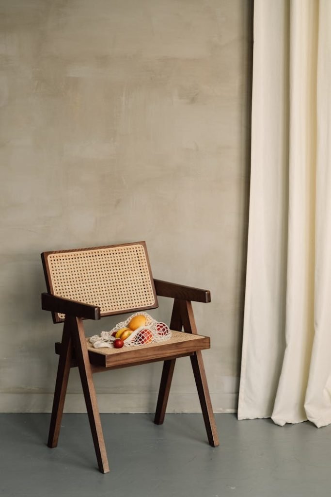 Wooden chair with a net bag of fruits against a neutral wall and curtain.