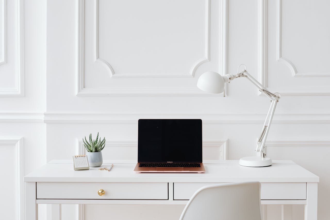 Elegant minimalist desk setup with laptop and white lamp in a bright room.