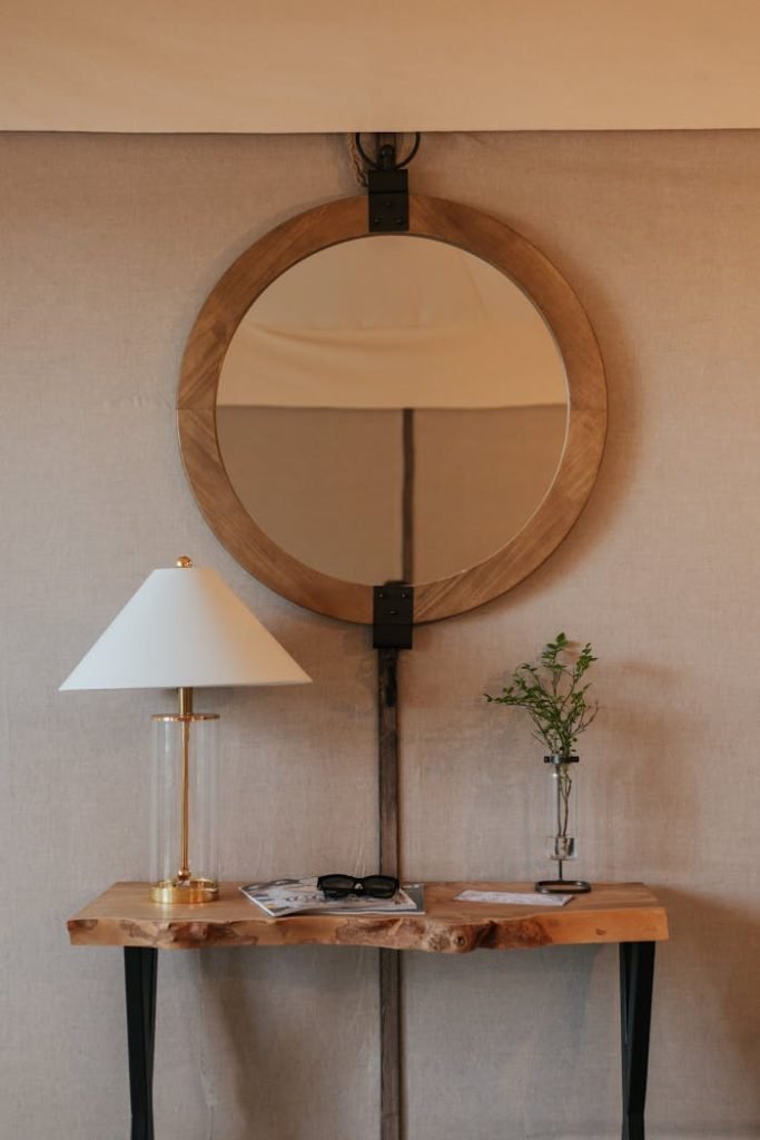 Stylish home interior featuring a round wooden mirror, modern lamp, and elegant decor on a wooden console table.